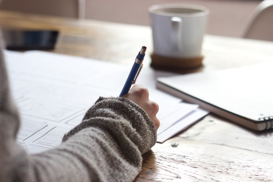 Lady holding a pen writing notes into a journal